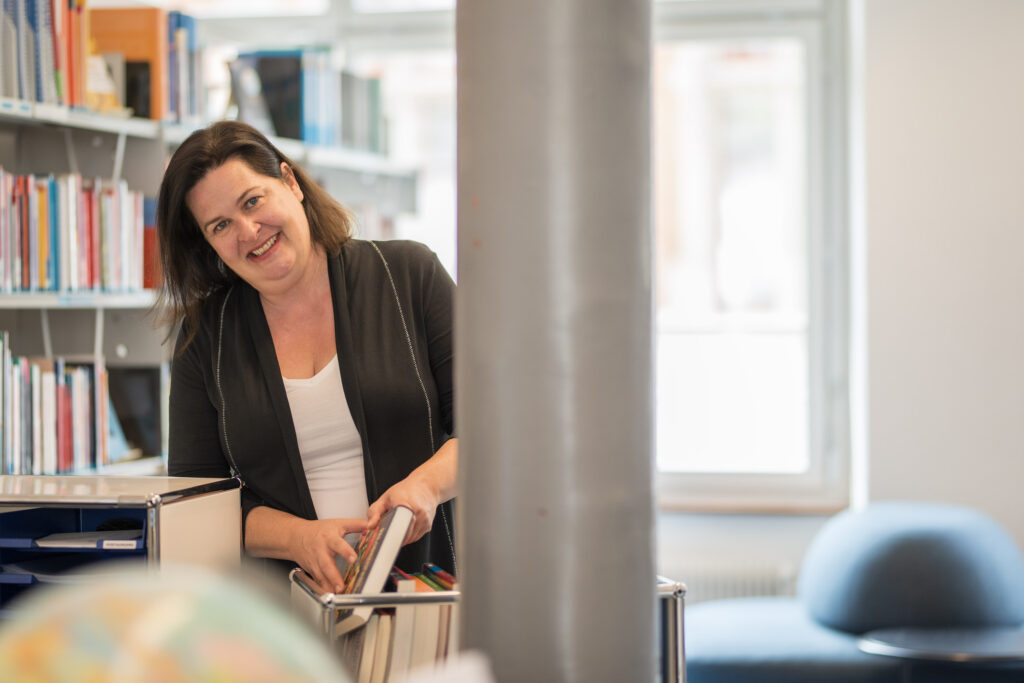 Das Bild zeigt die Mediotheksleiterin Verena Ben Othman in der Mediothek. Sie unterstützt mit Kompetenz und Herz Lehrpersonen, Lernende und Studierende bei Recherche, Fragen und Unsicherheiten.