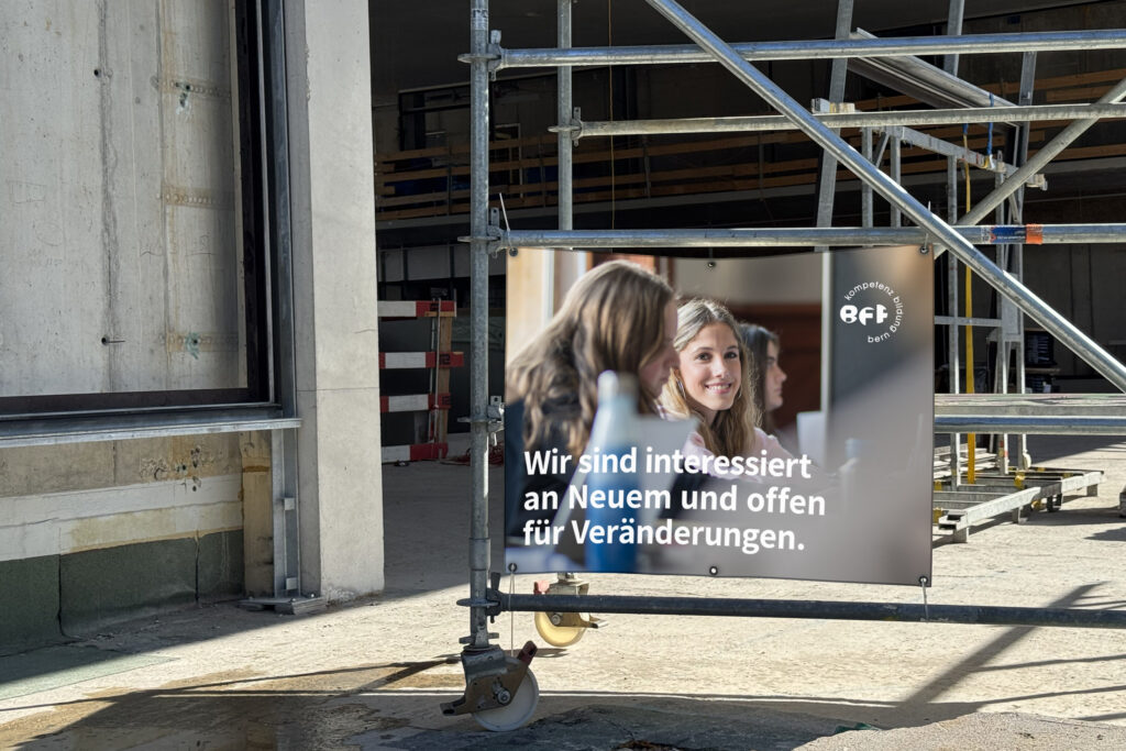 Das Bild zeigt das Leitbildplakat 2025, das an einem Gerüst in einer Baustelle angebracht ist.